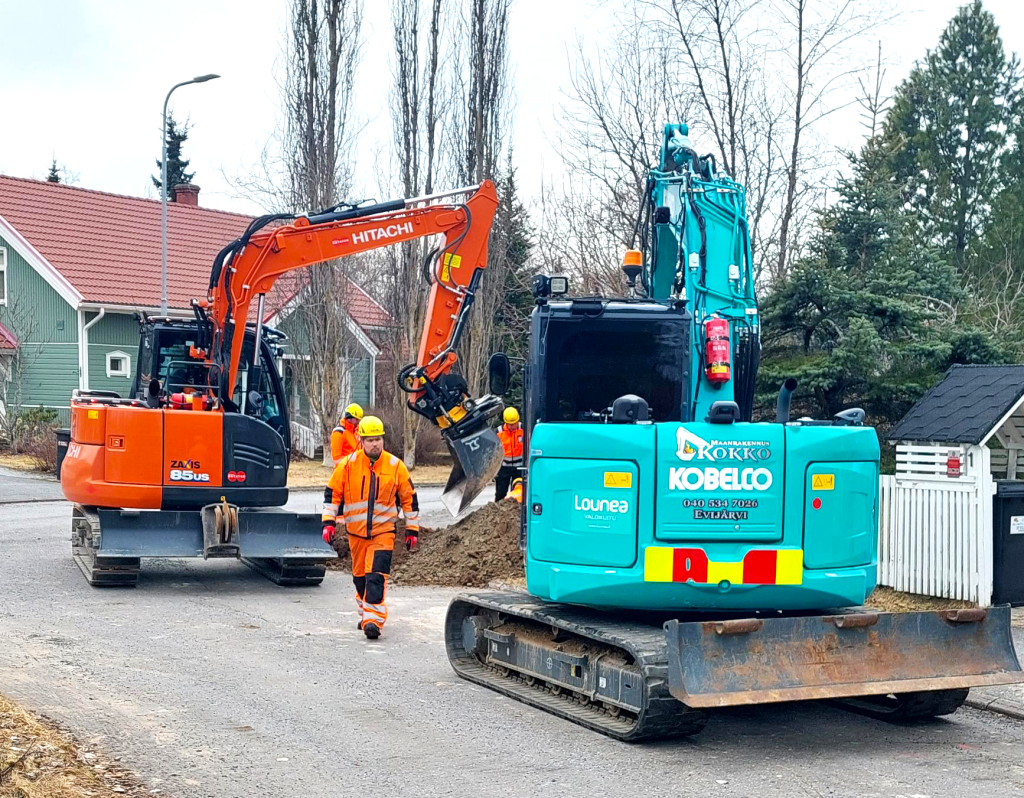 Kaksi kaivinkonetta ja työmies kaivamassa valokuitua kadulla